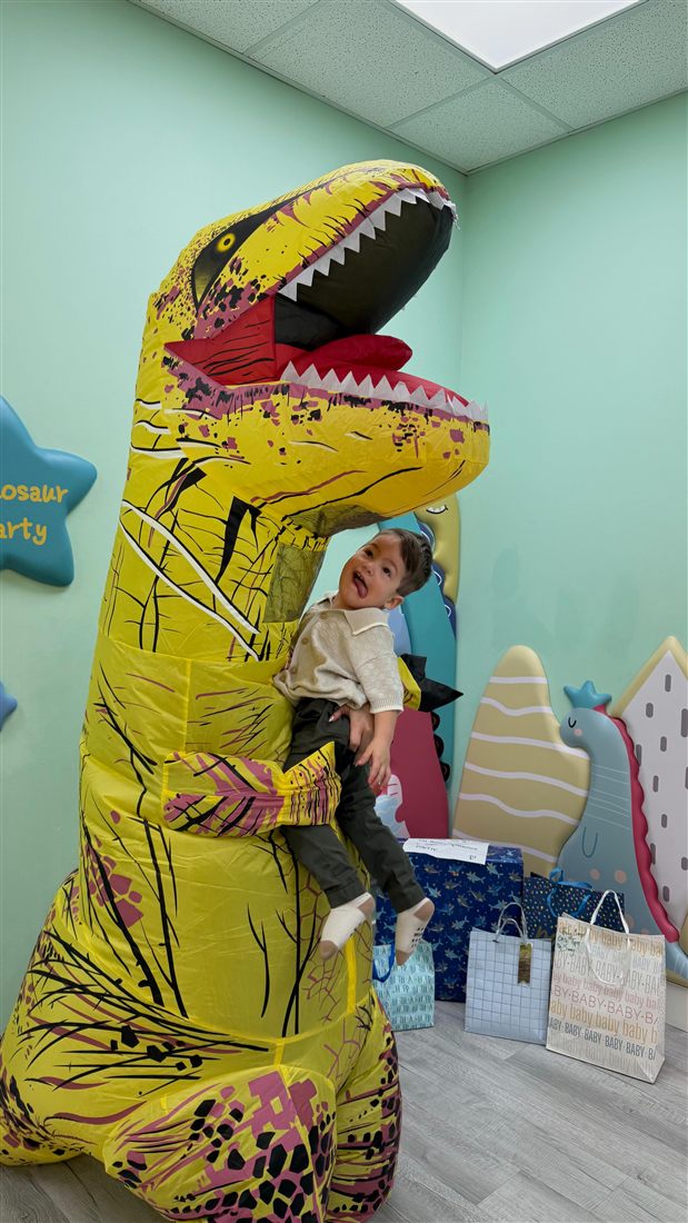 Toddler laughing while being hugged by a host in a tall yellow dinosaur costume