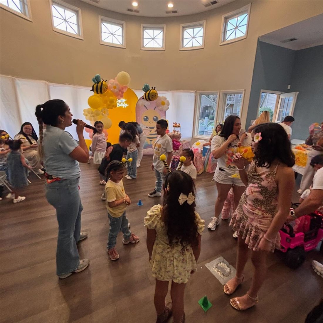Host with a microphone leading children in a game at a bee-themed birthday party