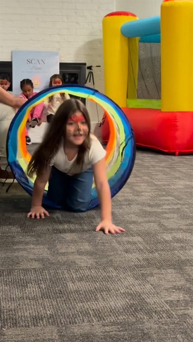 Child crawling out of a rainbow play tunnel during a party