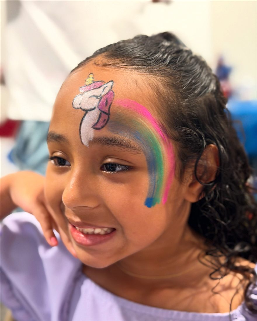 Girl smiling with a unicorn and rainbow painted on her forehead