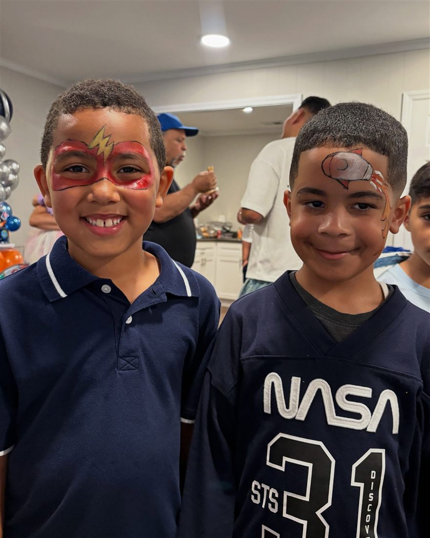 Two boys grinning with superhero masks painted on their faces