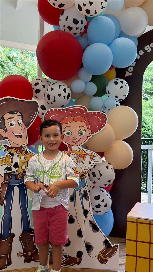 Boy smiling in front of Toy Story cutouts and a balloon arch